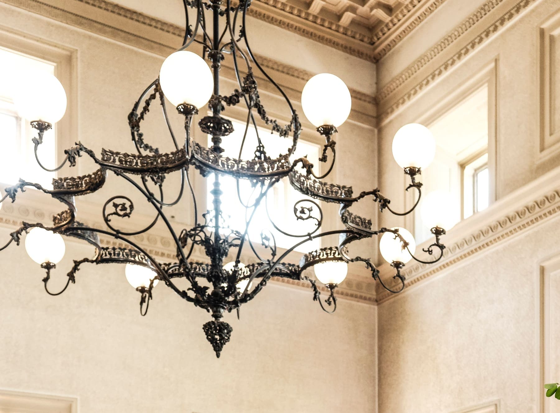 Wrought-iron chandelier with globe lights beneath a stucco ceiling