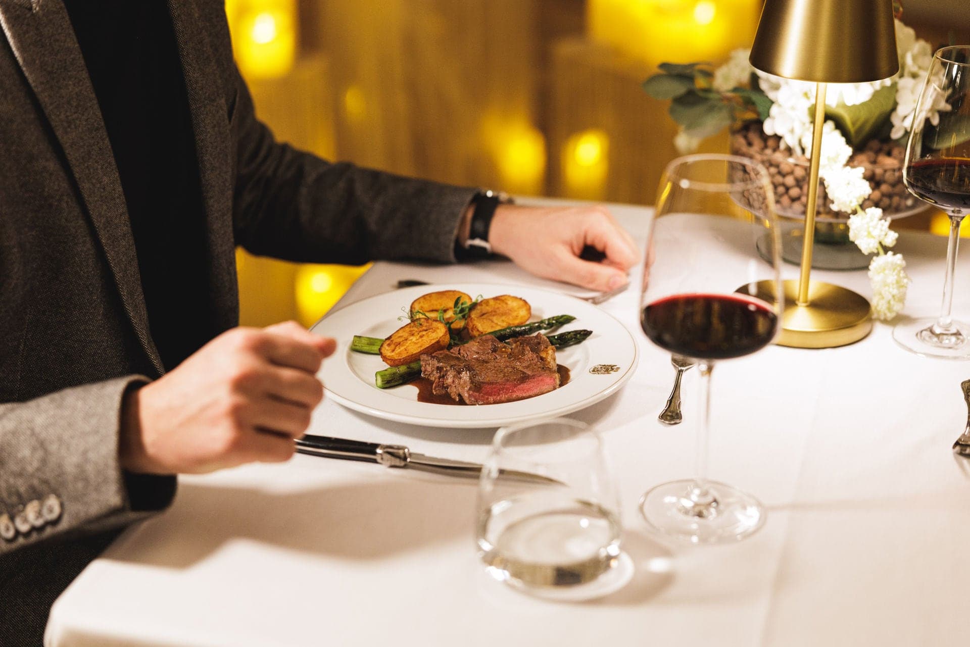 A guest at a laid table with fillet of beef and a glass of red wine