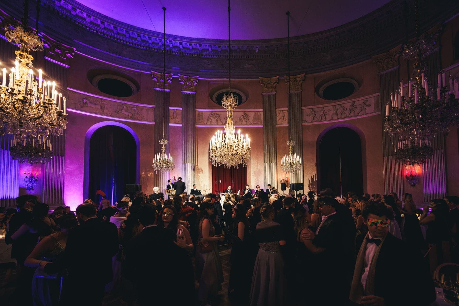 A packed dance floor in the Palais' main hall under violet light and crystal chandeliers