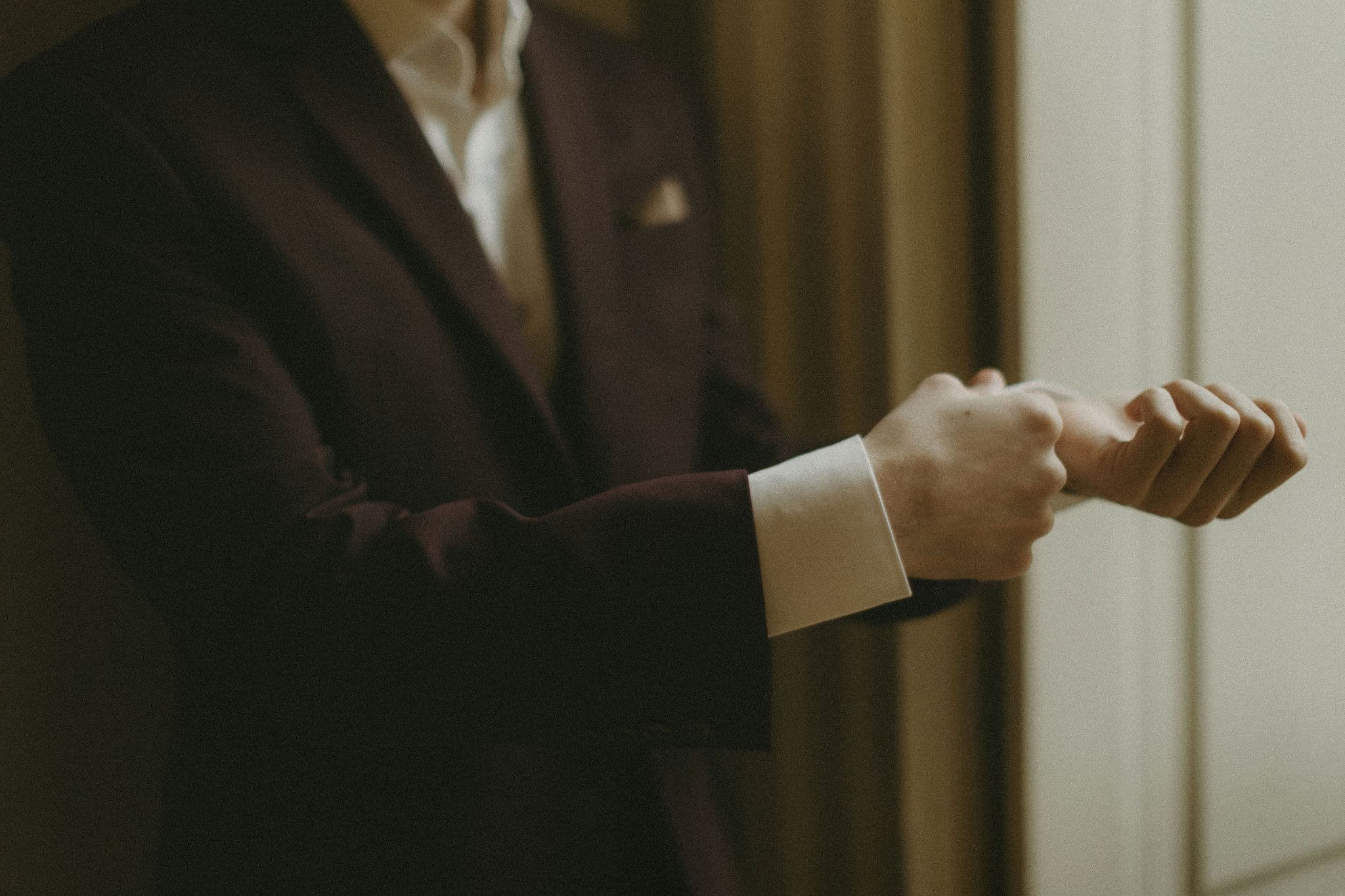 A guest in a dark velvet jacket adjusting the cuffs of his white shirt before the ball