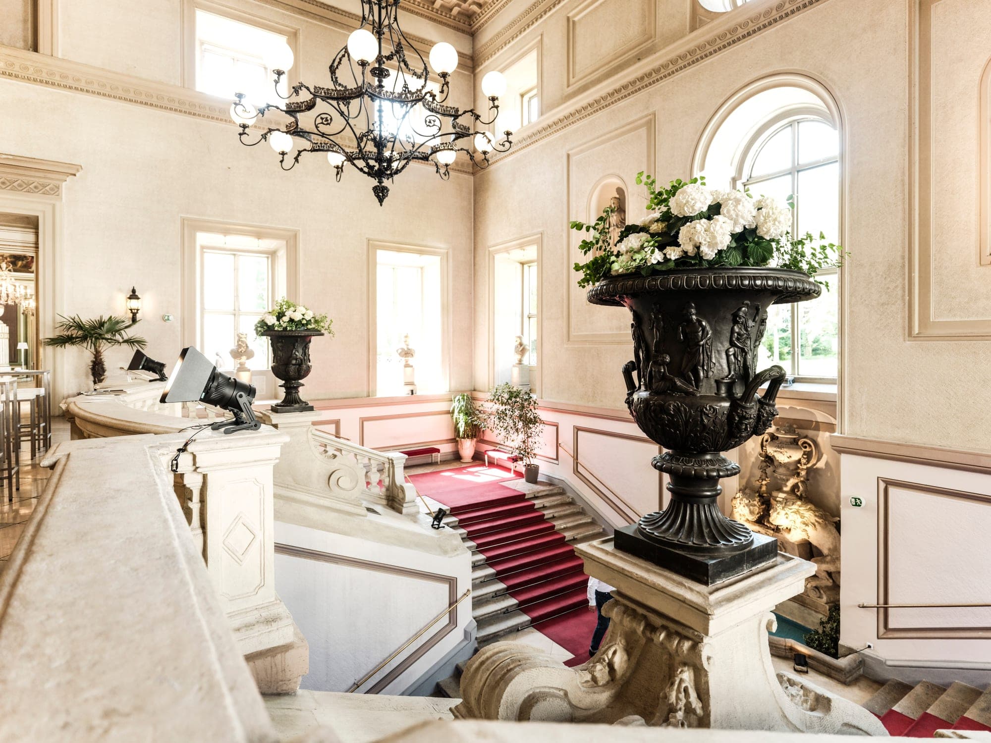 Grand staircase of Palais Auersperg with red carpet, chandelier and flower urn