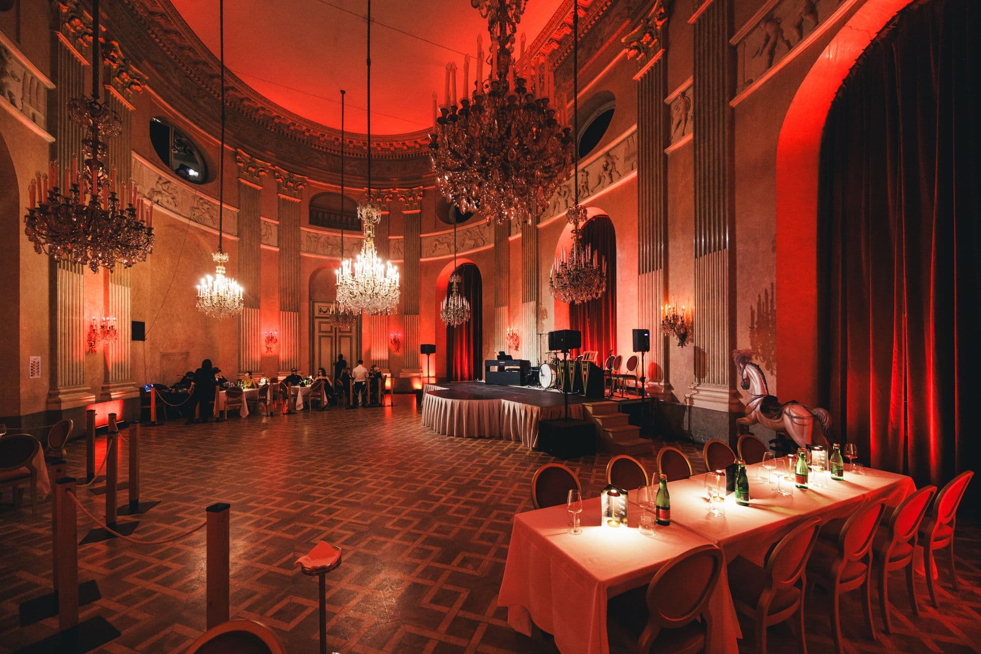 The round main hall with chandeliers in warm red light, candlelit tables