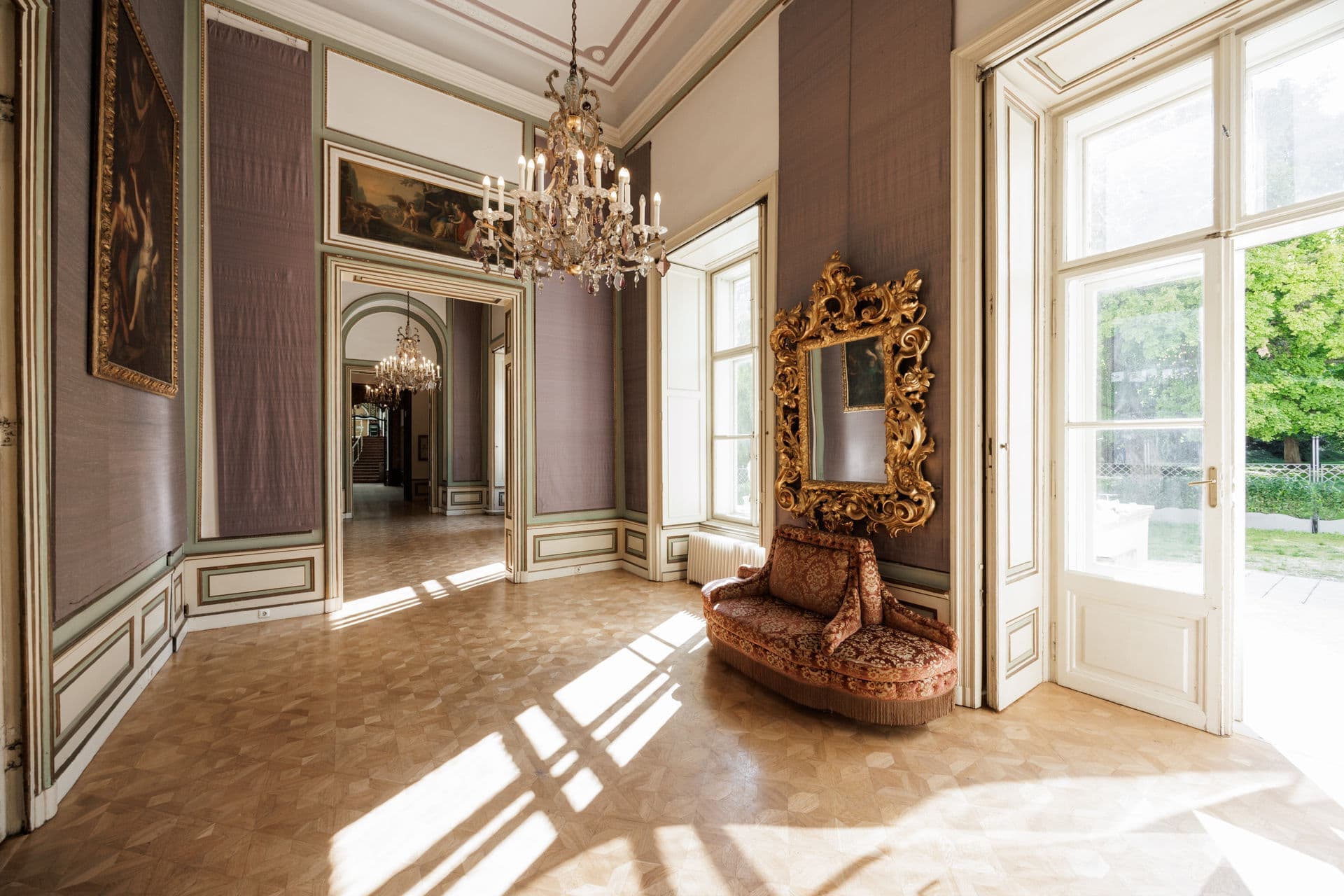 Bright salon with a crystal chandelier, gilded mirror and tall windows
