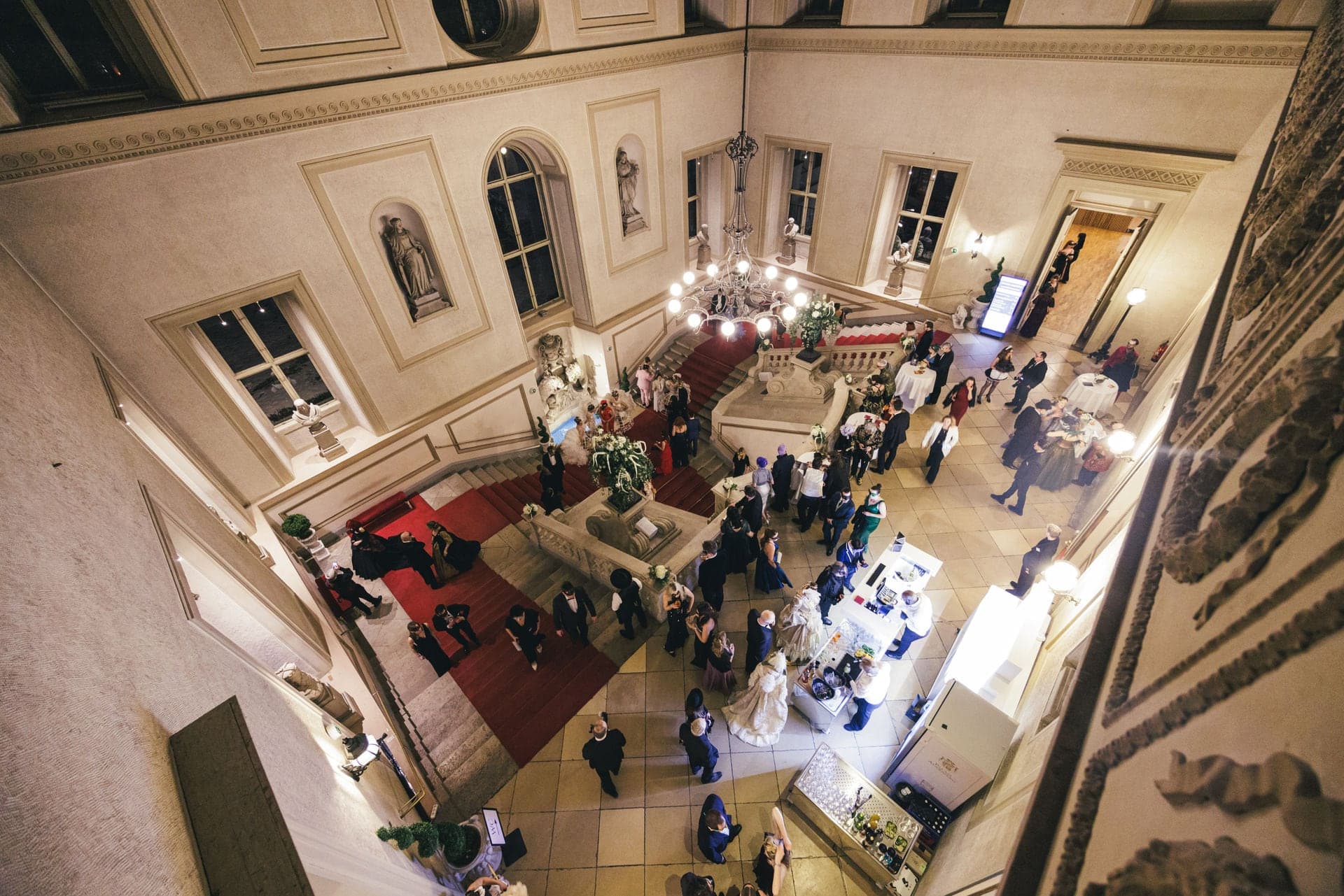 View from above onto the grand staircase with red carpet and arriving guests